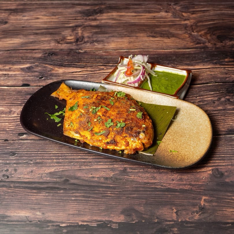 Whole grilled Indian fish, garnished with herbs, served with green chutney and onion salad.
