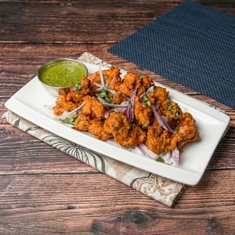 Mauli's Indian chicken pakora, garnished with red onions and cilantro, served with green chutney.