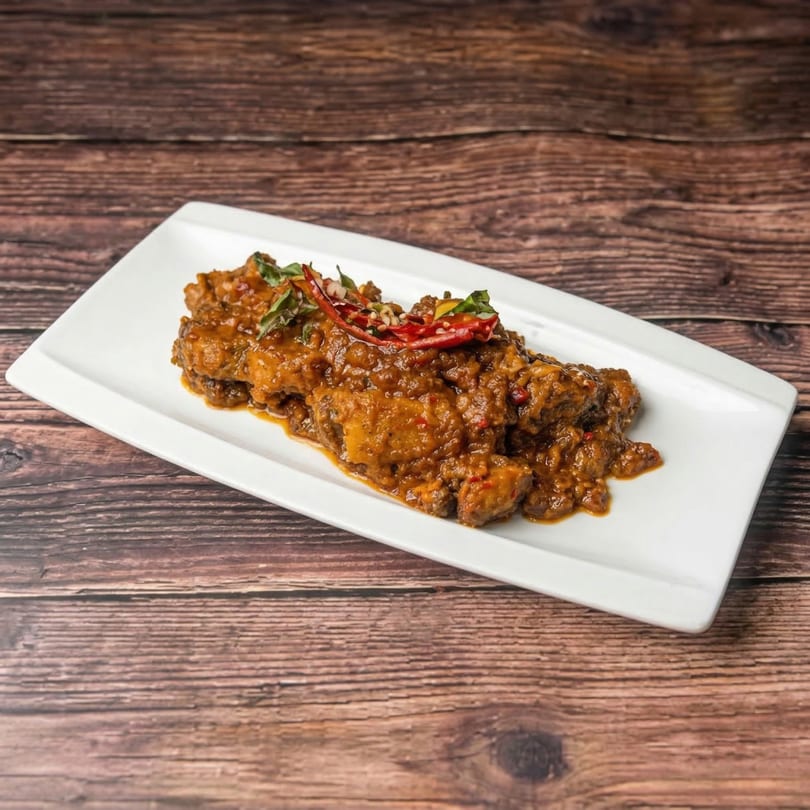 Indian chicken curry with red chilies and green herbs on a white rectangular plate.