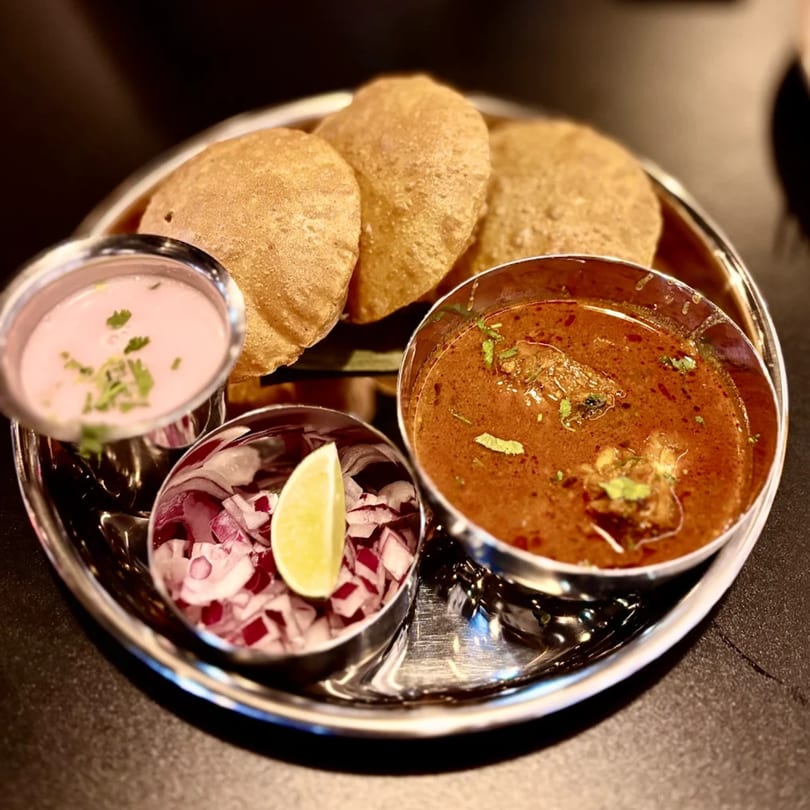 Mauli's Indian thali with puri, pink raita, red onion, lime, and a rich curry.